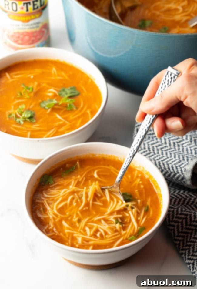 Two bowls of Sopa de Fideo with a pot of soup in the background. In the foreground, a hand holds a spoon scooping up a bite of soup.