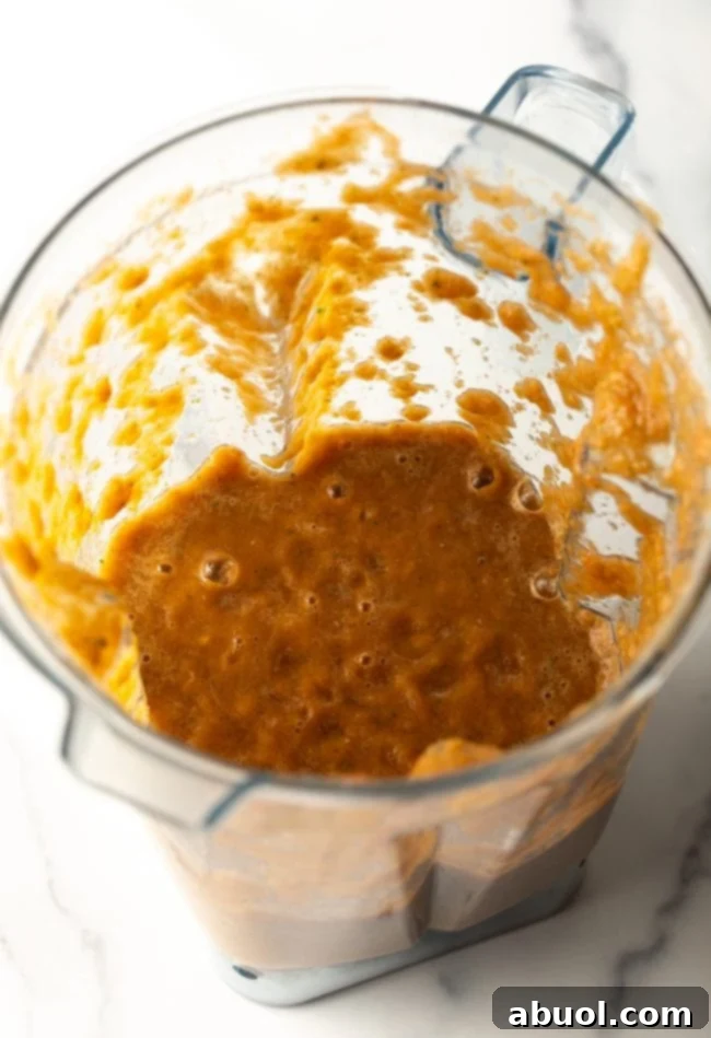 Top view of a blender jar containing a vibrant puree of tomato, garlic, jalapeño, and cilantro.