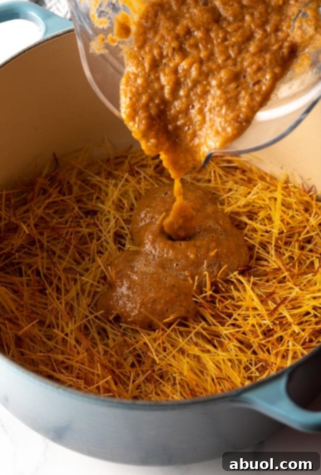 Pouring tomato puree from a blender jar into a large pot with browned pasta noodles.