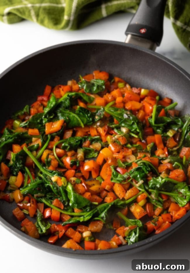 cast iron skillet with chopped red peppers and wilted spinach, ready for egg whites - a crucial step in preparing a healthy frittata.