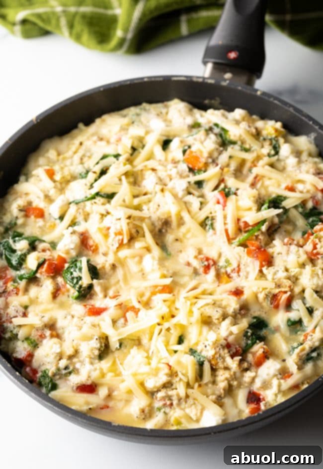 cast iron unbaked frittata with cheese sprinkled on top, ready to be baked to perfection.