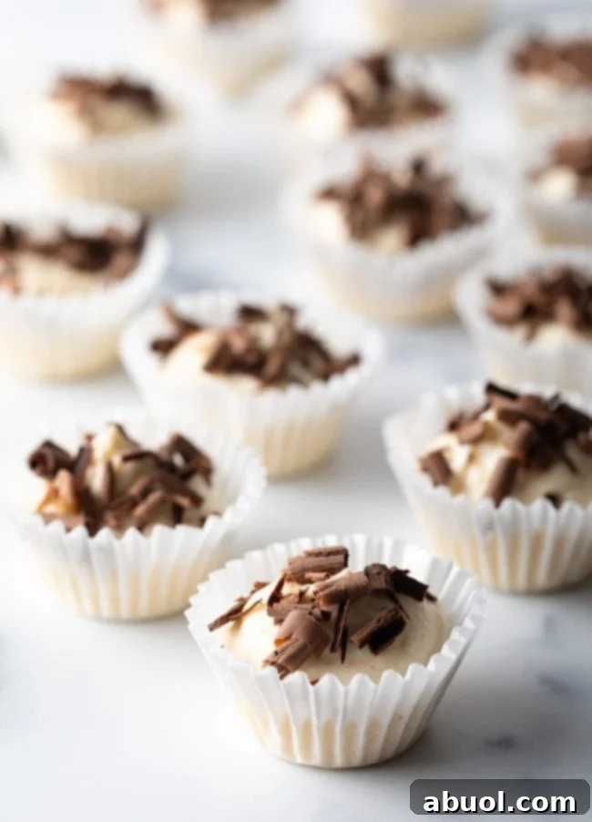 Close view of several no-bake keto cheesecake bites in small paper cups on a marble background with chocolate shavings on top.