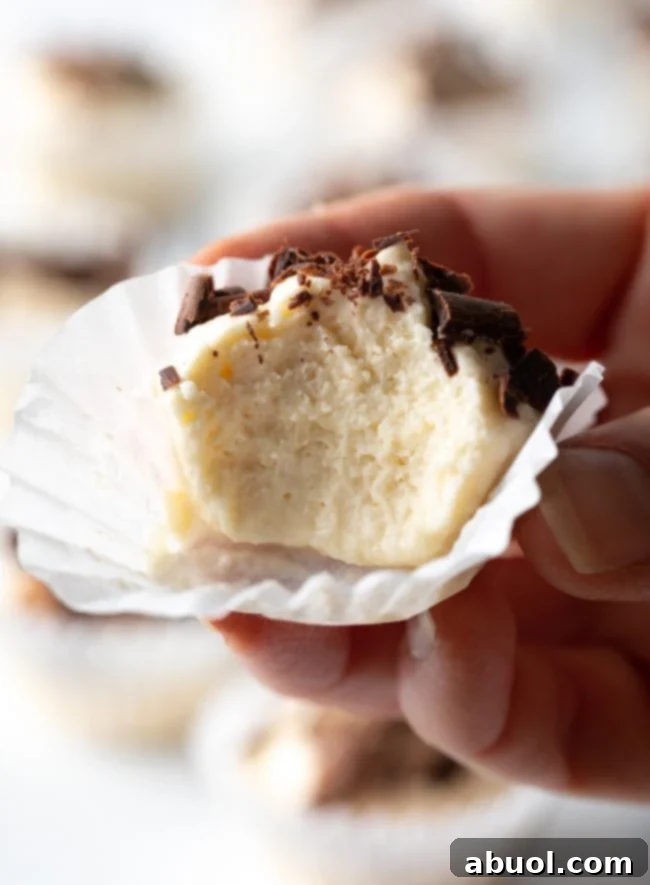 Hand holding keto cream cheese fat bomb in paper wrapping with bite taken out, showing close to camera.