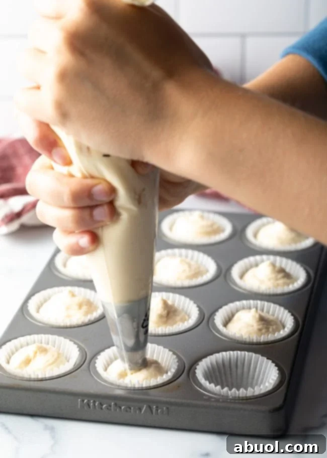 Hands with a piping bag, piping low carb keto cheesecake mixture into mini muffins pan.