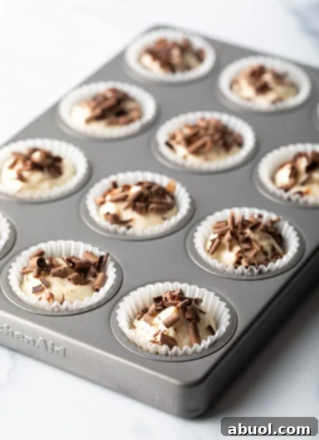 Mini muffin tin with white paper liners filled with keto cheesecake bites topped with chocolate shavings.