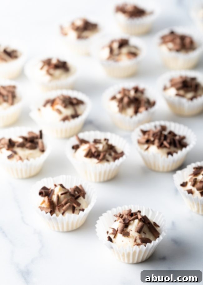 Pulled out view of a dozen mini cream cheese and chocolate bites in paper liners on a marble background.