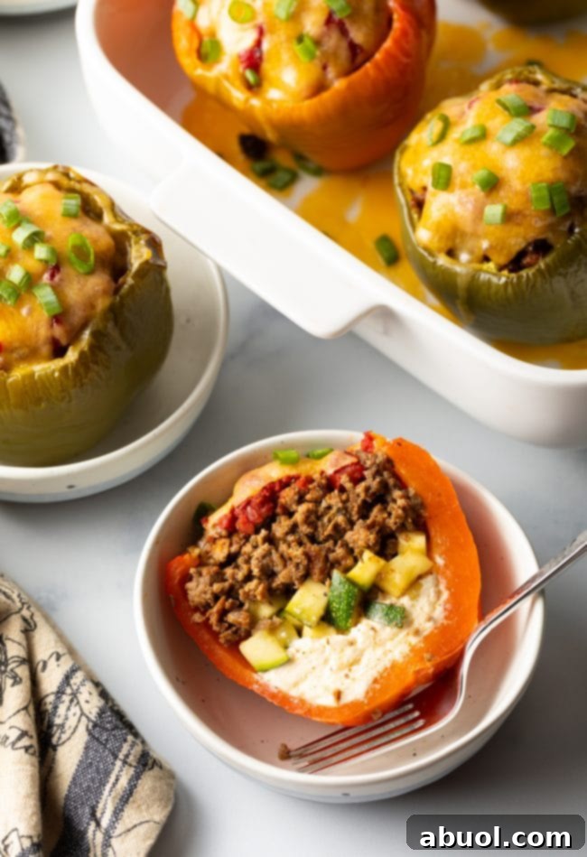 Top view keto stuffed peppers without rice, one cut in half to show ground beef, zucchini, and cream cheese, set in a white bowl.