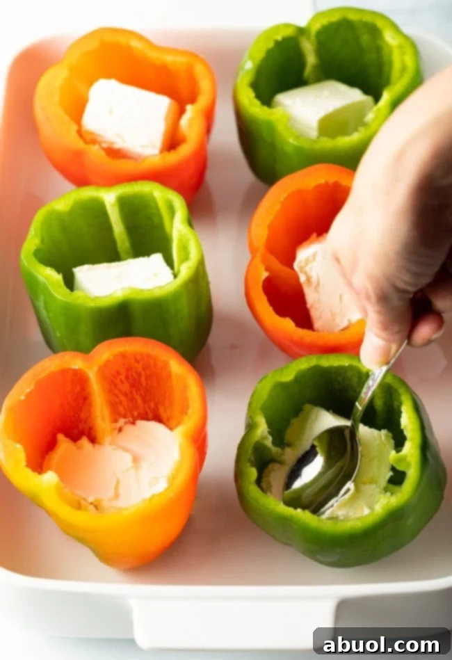 Hand using a spoon to press cream cheese into each pepper cavity.