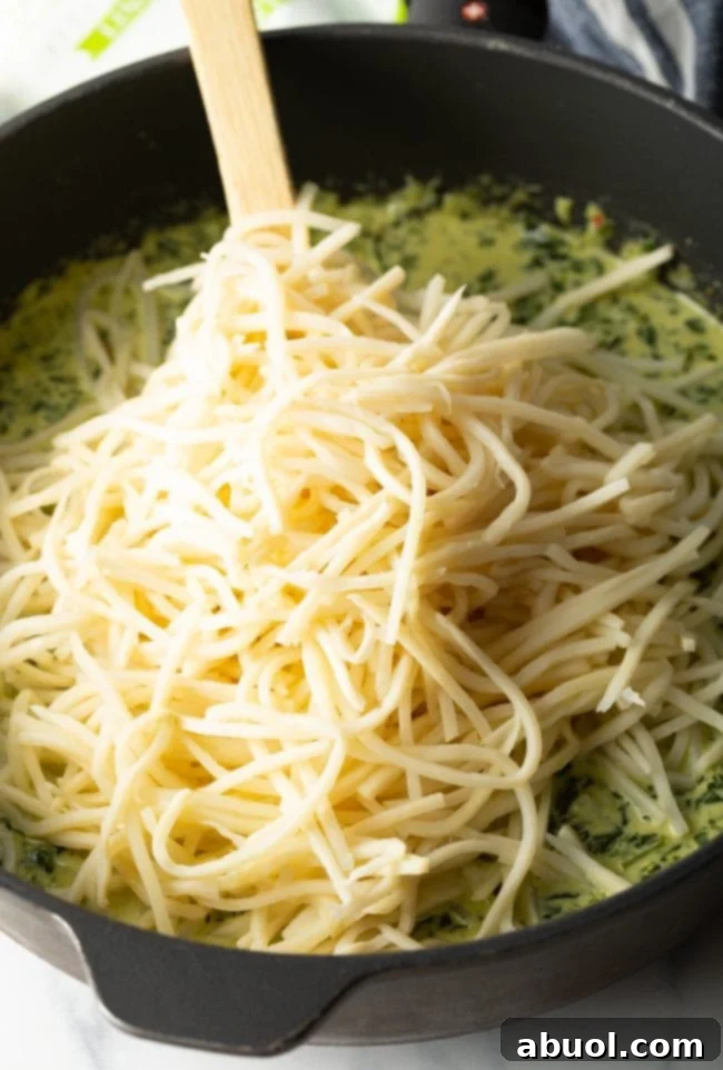 Hearts of palm pasta being added to the creamy spinach sauce in a skillet, ready to be combined.