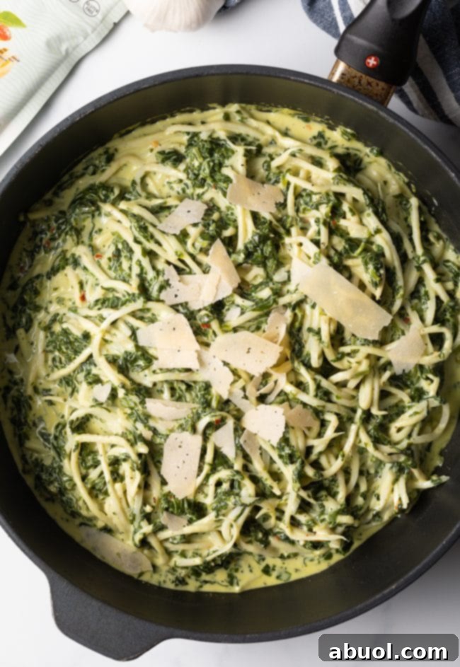 Top view of hearts of palm pasta with spinach cream sauce in a skillet, garnished with shaved Parmesan cheese.