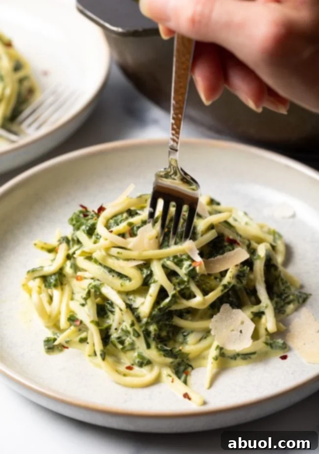 A hand twirling vegetarian spinach creamy pasta sauce on gluten-free hearts of palm noodles with a fork.