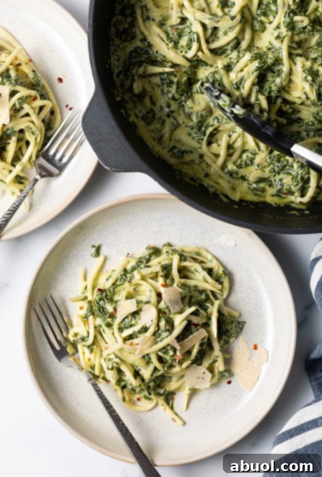 Top view of two plates of hearts of palm pasta with spinach cream sauce, with a skillet containing more pasta in the background.