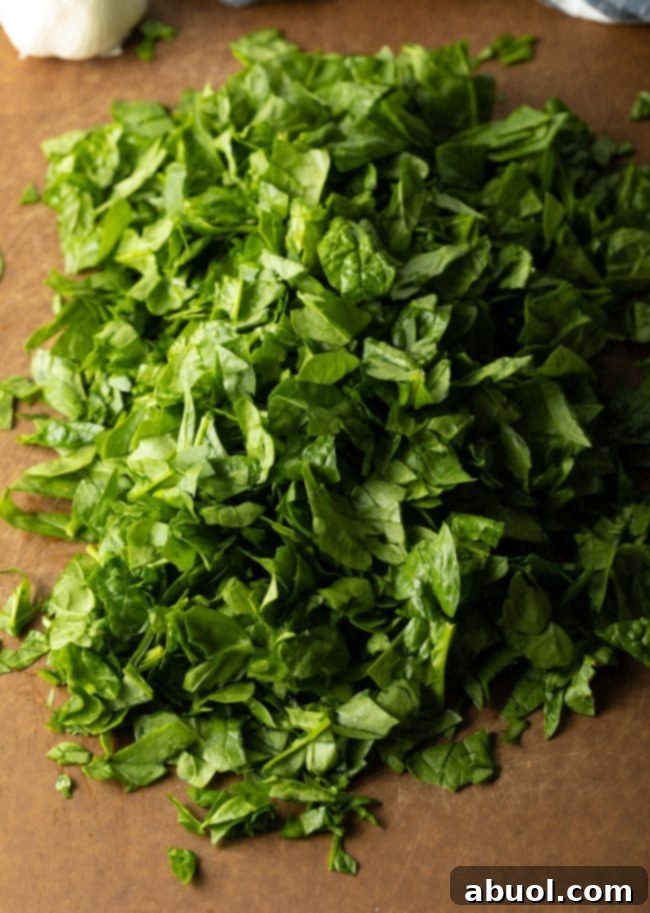 Fresh baby spinach, roughly chopped, on a wooden cutting board.