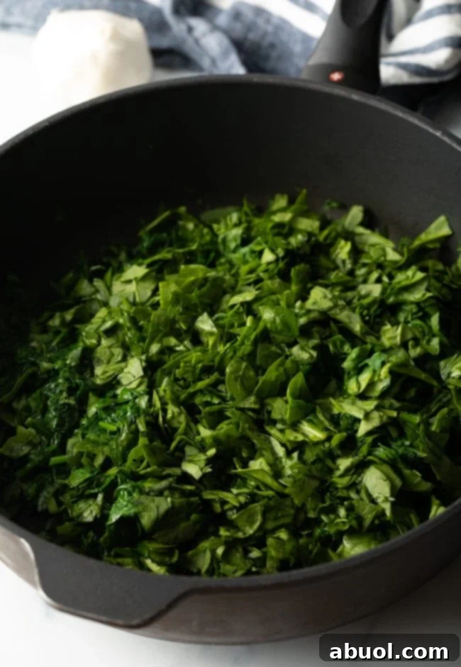 Chopped spinach wilting in a cast iron pan, ready for the creamy sauce ingredients.