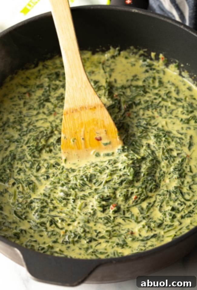 The creamy spinach sauce simmering in a skillet, stirred with a wooden spoon, reaching a thick consistency.