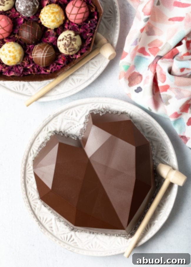 Top-down view of a beautifully presented heart-shaped chocolate box on a white plate with a miniature hammer, alongside an open bottom half filled with delightful truffles in the upper left corner.