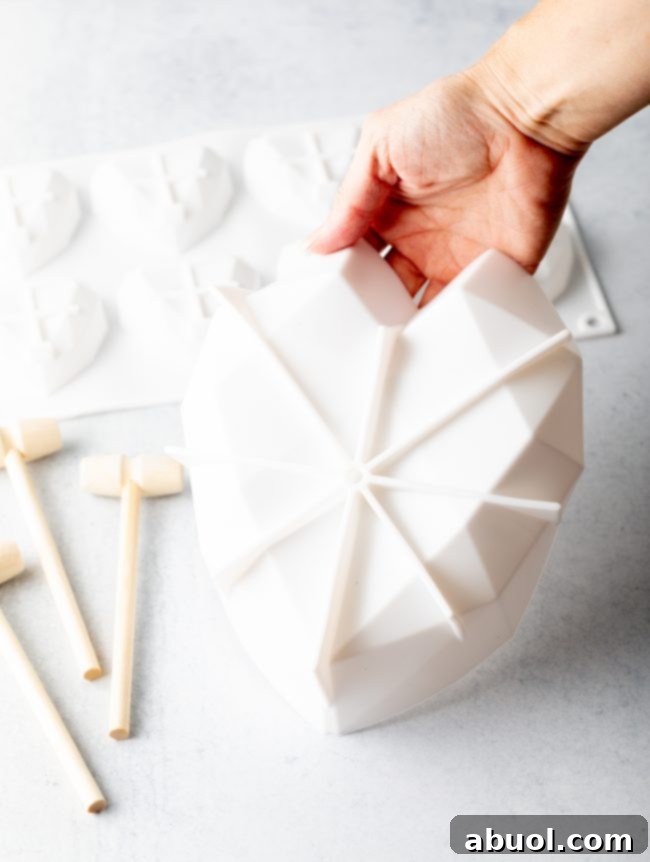A hand gently holding a white silicone heart shell mold, a crucial piece of equipment for crafting a DIY breakable chocolate heart.