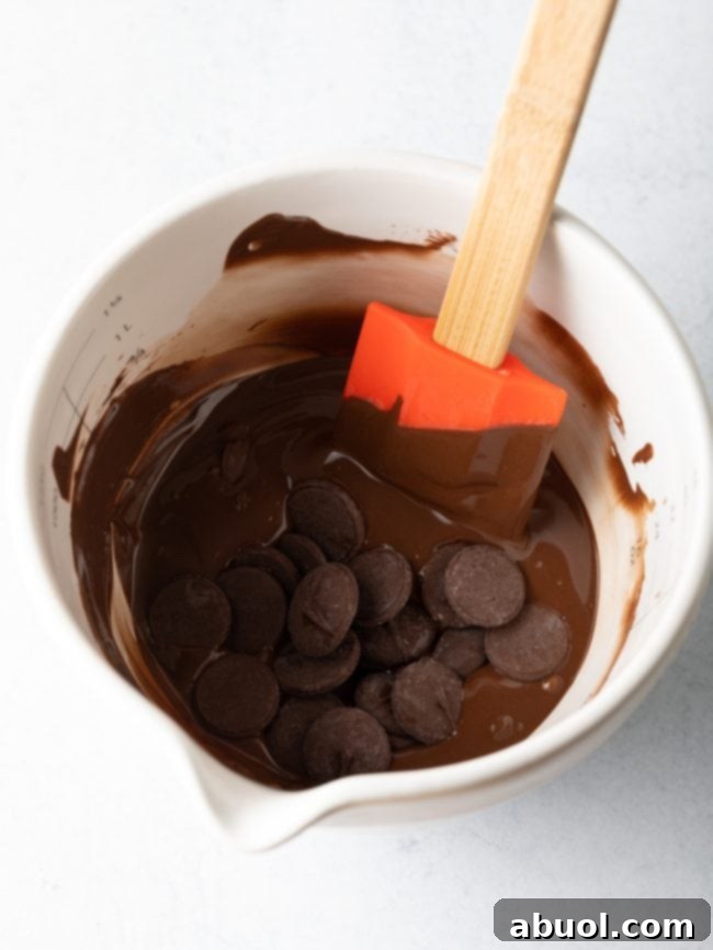 Melted chocolate wafers being stirred smoothly in a white measuring cup with a spatula, illustrating the ideal consistency for coating heart molds.