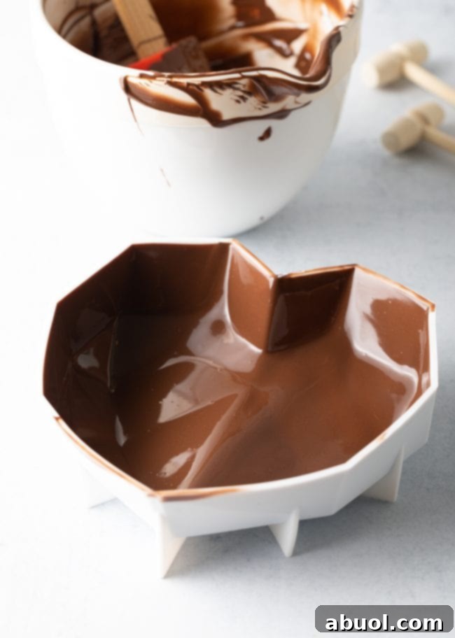 Silicone heart mold displaying its inside walls thoroughly coated with a thick, even layer of melted chocolate, indicating the successful application of the second reinforcing coat.