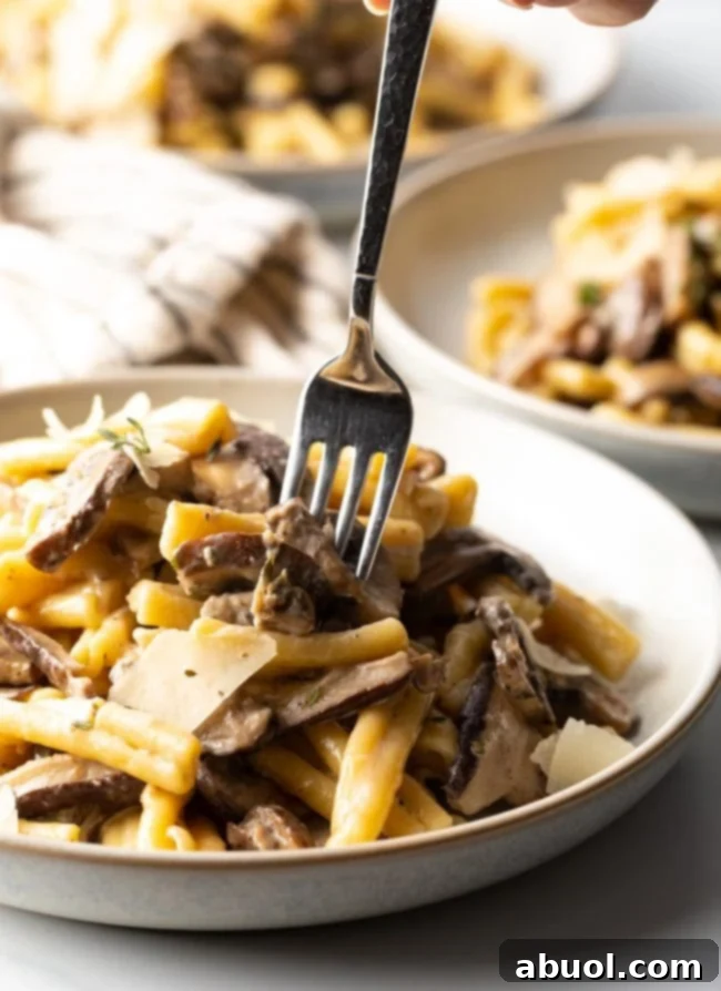 A fork taking a bite of mushrooms and noodles from a bowl of creamy pasta.