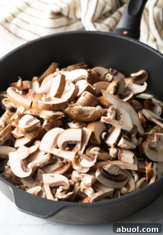Sliced mushrooms simmering in a deep skillet, releasing their juices.