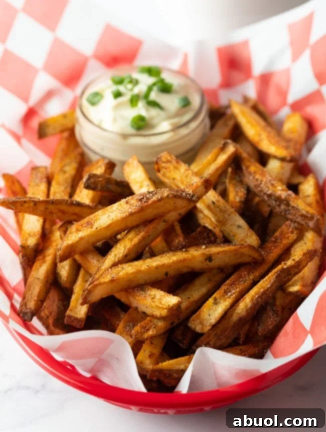 Close view of basket of seasoning fries with cup of sauce in the background.