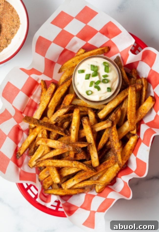Top view spicy Cajun fries in a basket with sauce in a small cup of sauce.