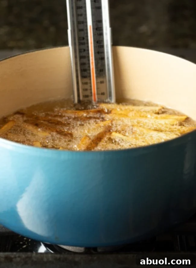Thermometer clipped to dutch oven filled with hot oil while frying potatoes. 