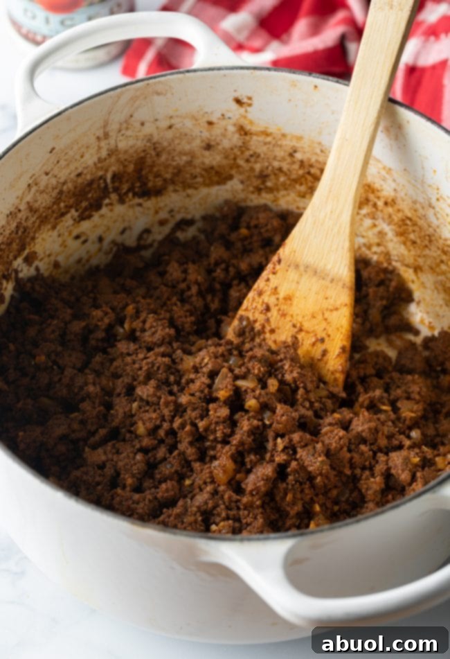 Ground beef browned in a large pot with wooden spoon.