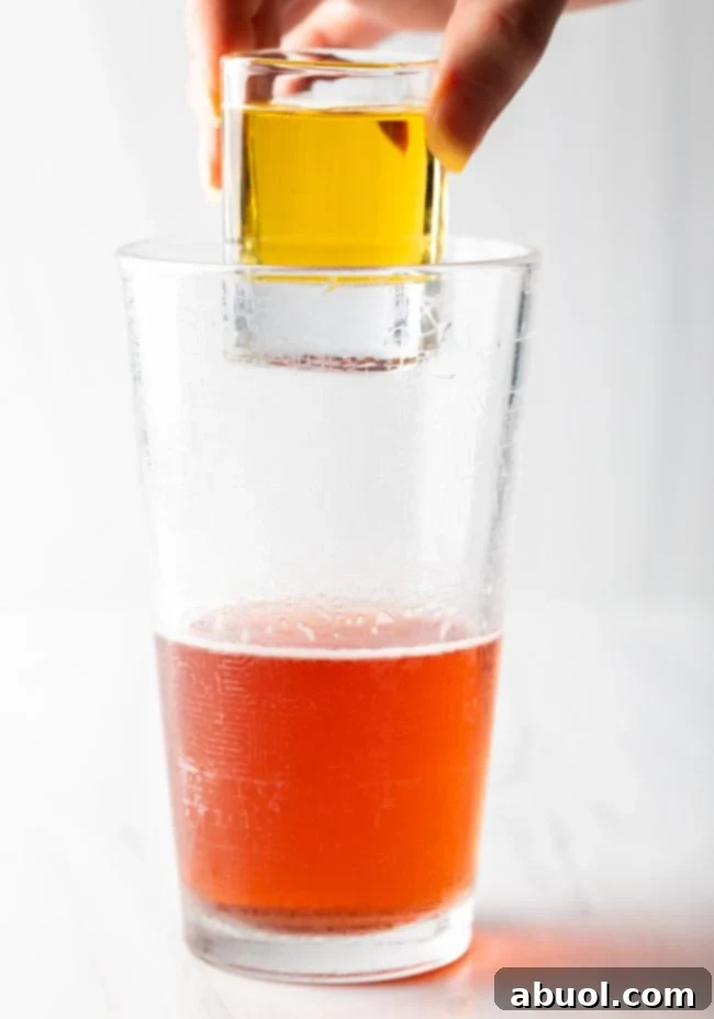 A hand holds a red bull shot above the glass for Vegas Bomb. 