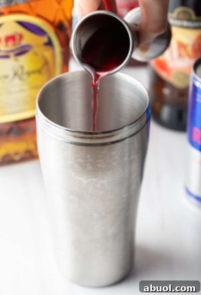 Closeup of hand pouring cranberry juice into a metal tumbler.
