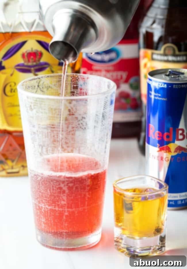 Shaker pouring Vegas bomb shot base into a tall glass with a shot of red bull on the side.
