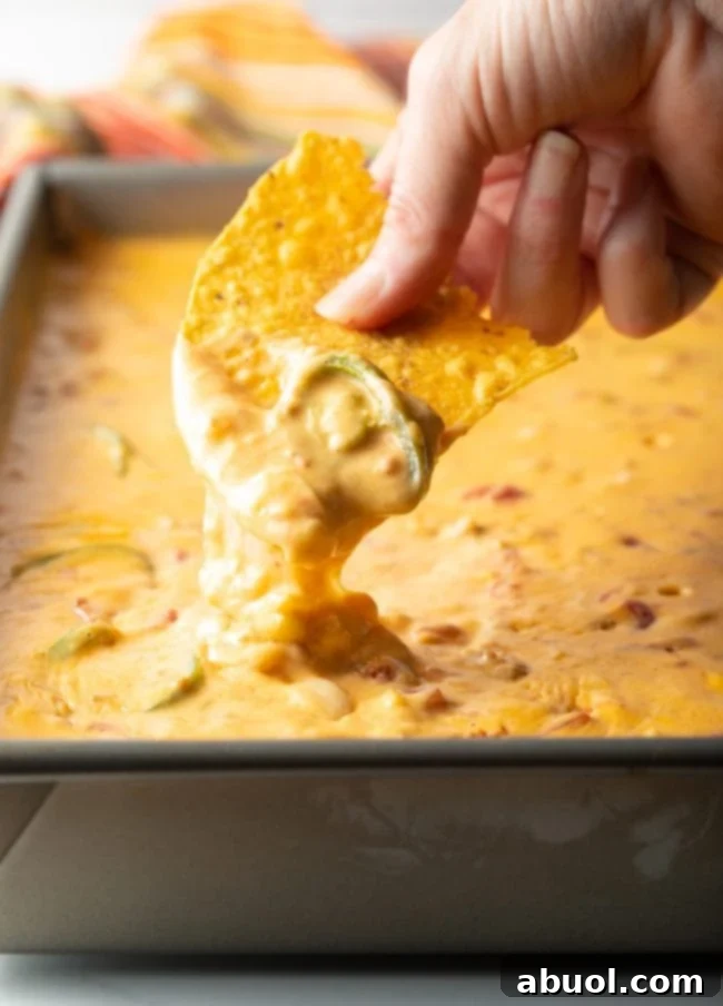 hand scooping smoked queso recipe with jalapeno for a large pan of dip