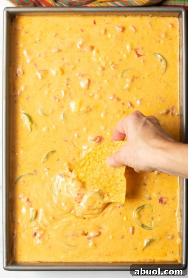top view smoked queso dip with hand dipping in a tortilla chip
