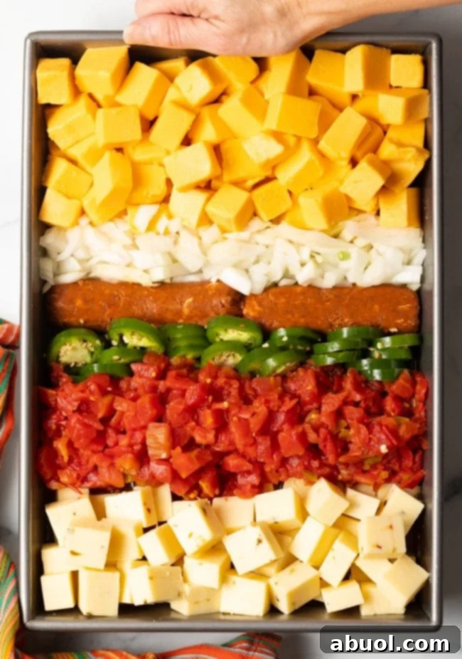 top view metal pan with rows of pepper jack cheese, rotel, sliced jalapenos, Mexican chorizo, onions, and velveeta cubes