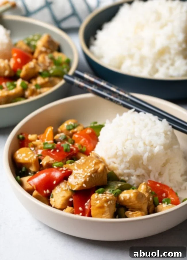 A beautifully presented bowl of Chinese garlic chicken with colorful bell peppers, perfectly portioned with a scoop of white rice on the side.