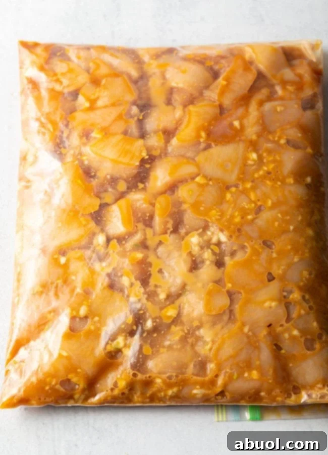 A top-down view of chicken pieces marinating in a flavorful sauce inside a clear plastic zip-top bag, ready for refrigeration.