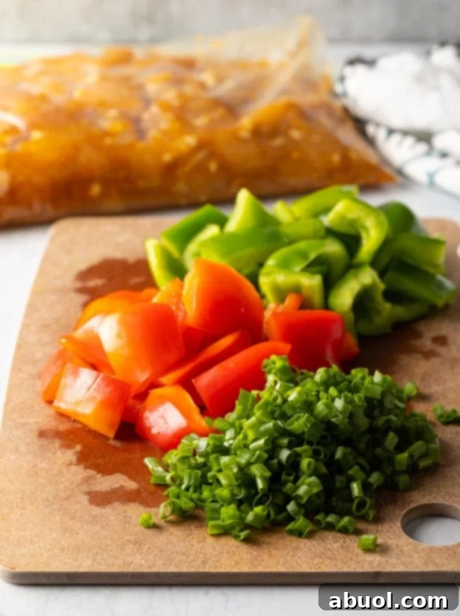 A cutting board laden with freshly chopped red and green bell peppers, accompanied by neatly sliced scallions, all prepped for stir-frying.