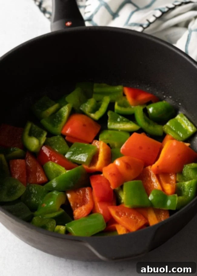 Vibrant red and green bell peppers searing in a large black skillet over high heat, preparing for the stir-fry.
