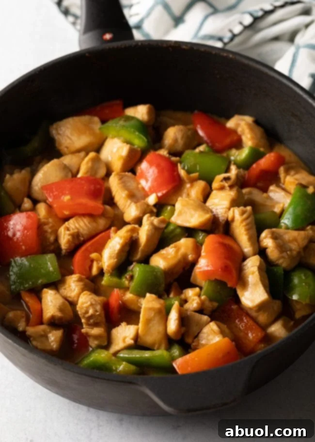 Succulent marinated chicken pieces and tender-crisp red and green bell peppers cooking together in a rich, glossy sauce in a large skillet.