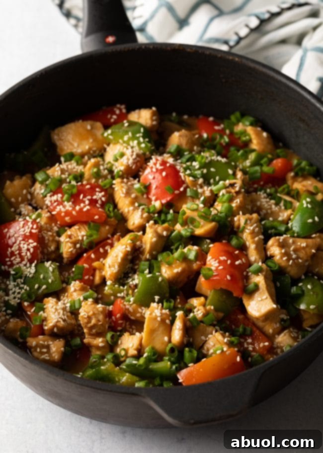 A top-down view of a finished skillet of Chinese garlic chicken and bell peppers, generously garnished with fresh sliced scallions and toasted sesame seeds, ready to be served.