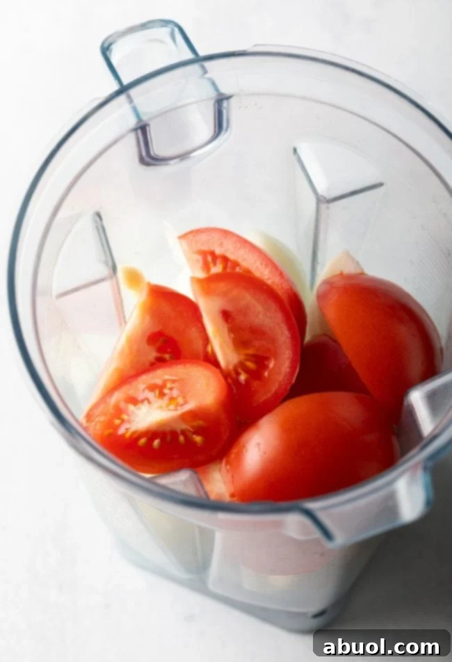 Sweet onions, ripe tomatoes, fresh ginger, and garlic cloves arranged in a blender, ready for making the creamy base of Maafe.