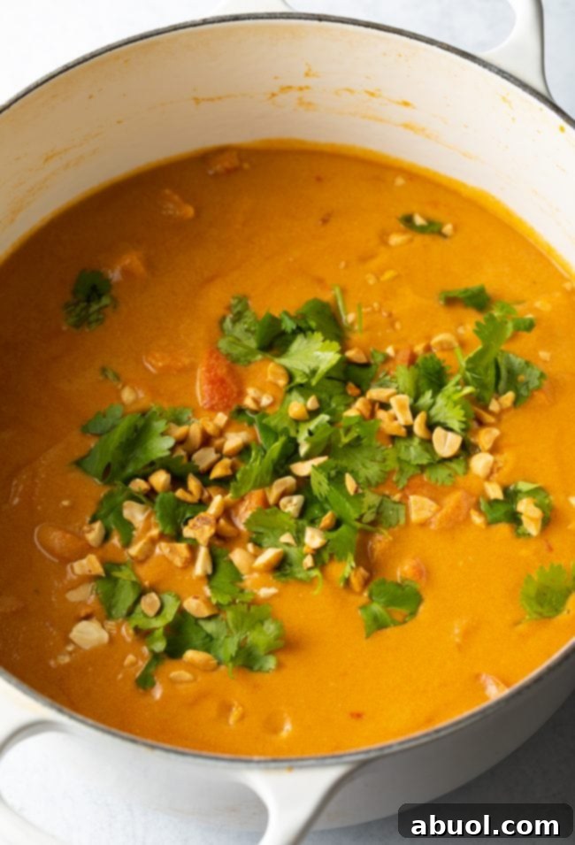 The finished West African Peanut Soup (Maafe) simmering in a large pot, garnished generously with fresh cilantro and crushed peanuts.