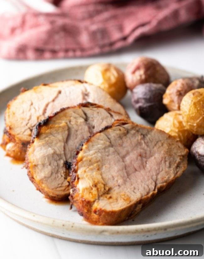 Side close view of sliced pork tenderloins on a white plate with small potatoes, highlighting the texture and juiciness.