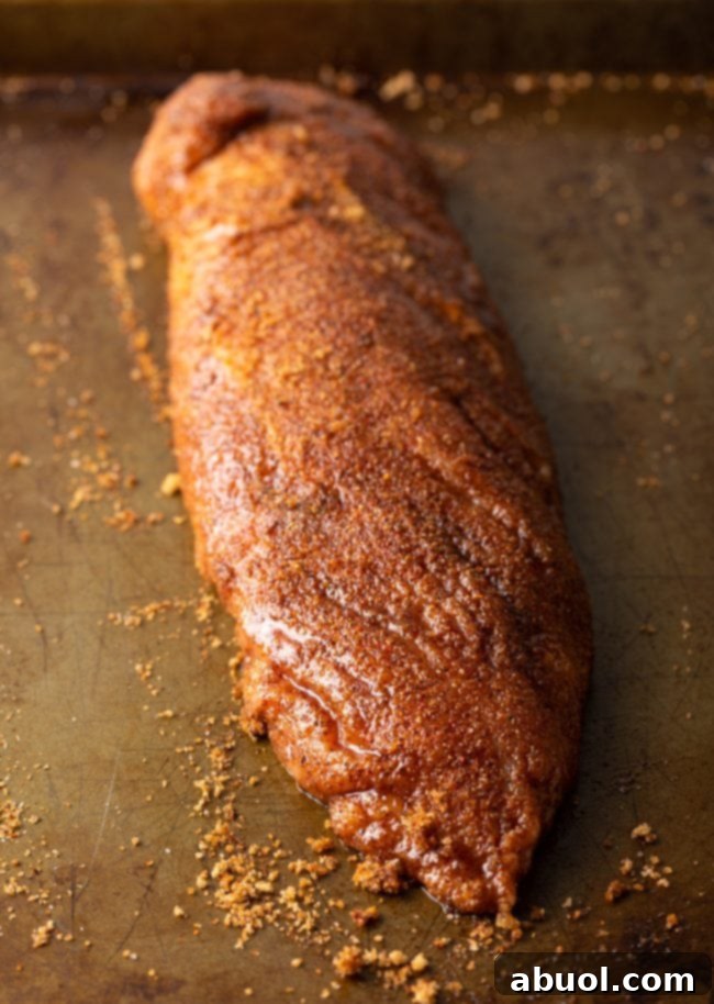 Raw pork loin completely covered in a rich spice rub, laid on a baking sheet.