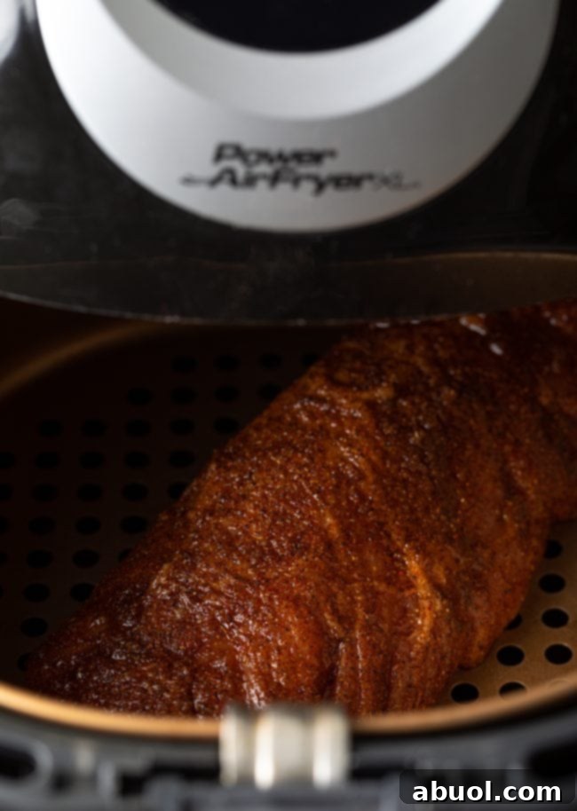 Spice-crusted pork loin cooking inside an air fryer basket, showing initial browning.