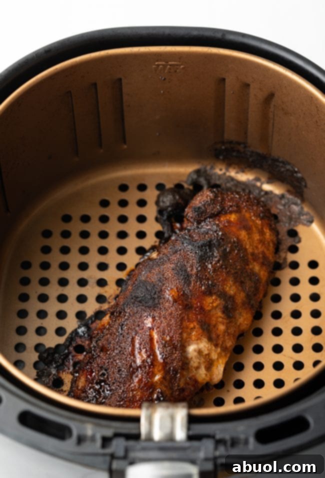 Cooked pork loin resting inside the air fryer basket, indicating readiness.