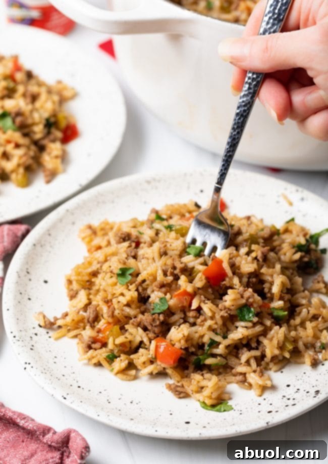 Plate of fried dirty rice with a hand taking a forkful.