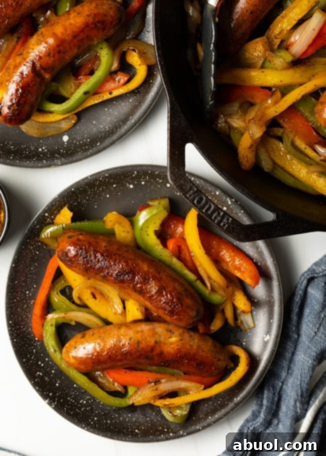 Top down view two plates with two links of cooked sausages, peppers, and onions on each plate.
