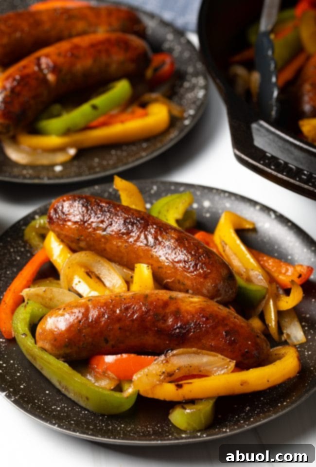 Side view two cooked sausage links with bell peppers and onions on a plate.